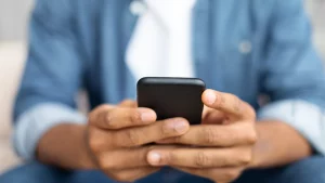Homem utilizando smartphone com foco nas mãos segurando o aparelho. A imagem transmite concentração e conectividade, ideal para ilustrar temas como tecnologia, aplicativos móveis, redes sociais, comunicação digital e uso de dispositivos móveis no dia a dia.